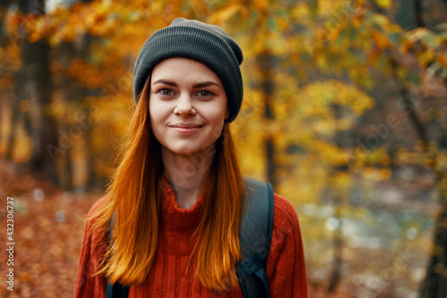 portrait of a beautiful woman in a hat sweater with a backpack on her back in the autumn forest in nature