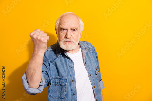 Photo of angry unhappy old man wear denim shirt raise fist argument problem isolated on yellow color background photo