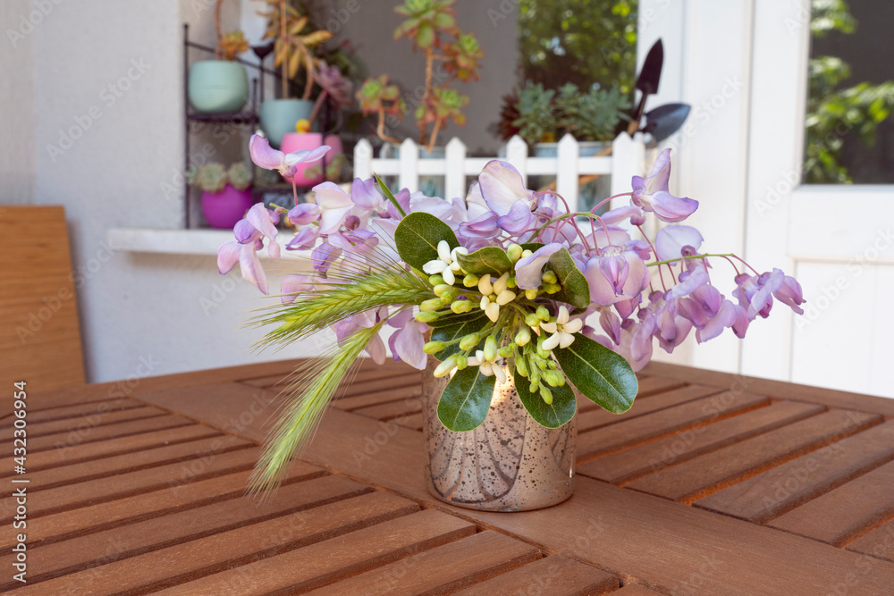 Fototapeta premium Lovely bouquet of wisteria on a wooden table on a balcony. Fells like summer. Succulents at background.