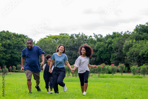 Happy mixed race family African father and Asian mother with two little daughter holding hands walking together in park. Mom and dad with child girl kid enjoy and having fun outdoor lifestyle activity