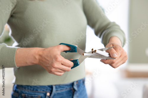 Female hands holding bunch of cigarettes and cutting them in halves with scissors