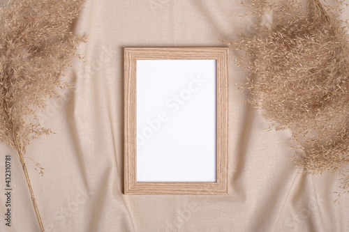 Picture frame with blank paper card mockup near to pampas dry grass on beige neutral colored textile
