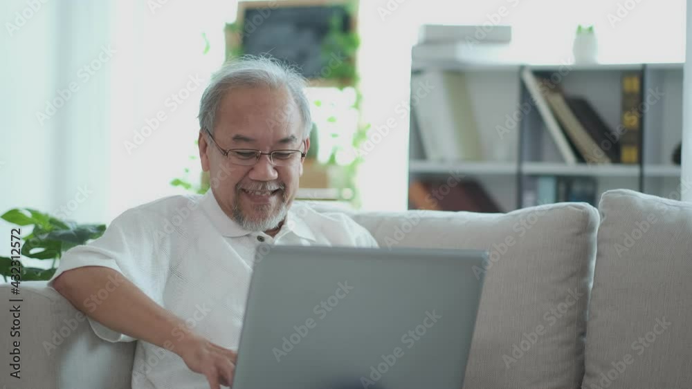Slow Motion. Smiling business senior elderly asian sit on sofa browsing, chatting and video call on laptop computer. lifestyle of retirement age concept. Slow Motion. Smiling business senior elderly asian sit on sofa browsing, chatting and video call on laptop computer. lifestyle of retirement age concept.