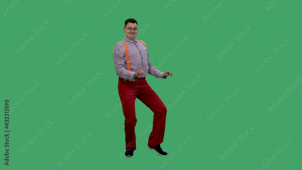 A man with a happy expression dances, moving his hips vigorously, and says something. Portrait of a man in glasses, in a plaid shirt with orange suspenders in the studio on a green screen. Slow motion