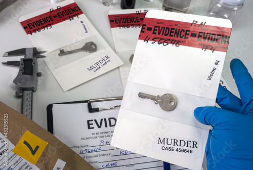 Police scientist holds sample bag with key of victim implicated in laboratory murder, concept image photo