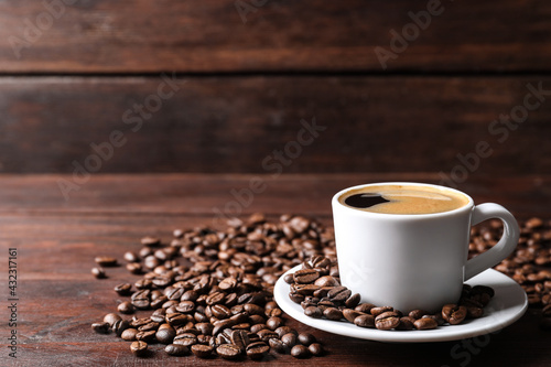 Cup of hot aromatic coffee and roasted beans on wooden table. Space for text