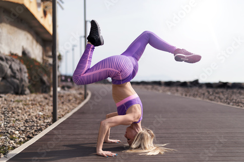 Girl trains in the city near the sea. She does fitness in yoga positions.