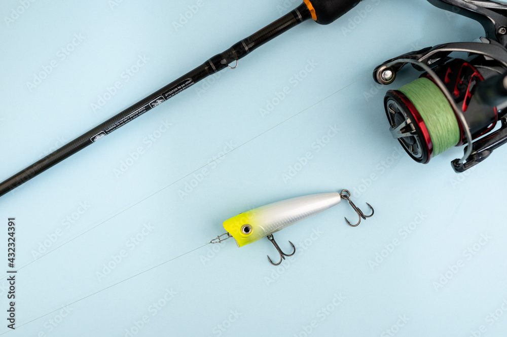 Bass fishing concept on the blue trendy background. Flat lay style. Fishing tackle, popper lure on the line.
