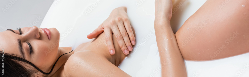 Fototapeta premium young woman relaxing in bath with milk while covering breast with hand, banner.