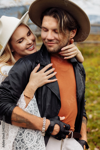 Portrait of adorable woman in white dress hugging handsome man, smiling. Gorgeous stylish marriage couple walking at the field, having a wedding photoshoot, spending weekends together