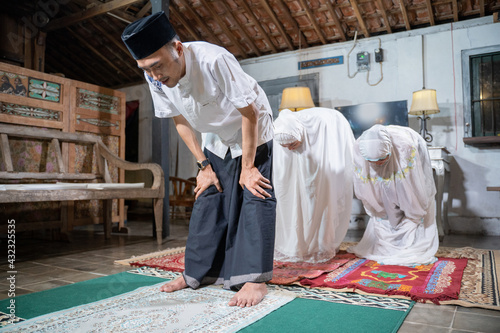 asian muslim family praying jamaah together at home. sholat or salah wearing white and hijab photo