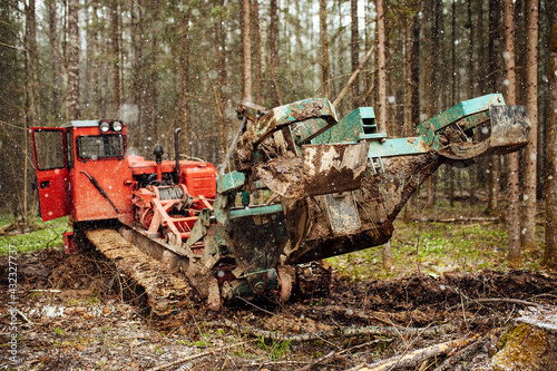 a crawler tractor is driving through a forest clearing. an industrial bulldozer is stuck in the mud. trucks are skidding in the ground