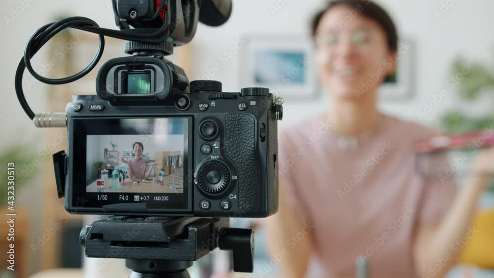 Make-up artist is recoding video showing cosmetic products on professional camera. Focus on videocamera screen while woman is blurred in background.