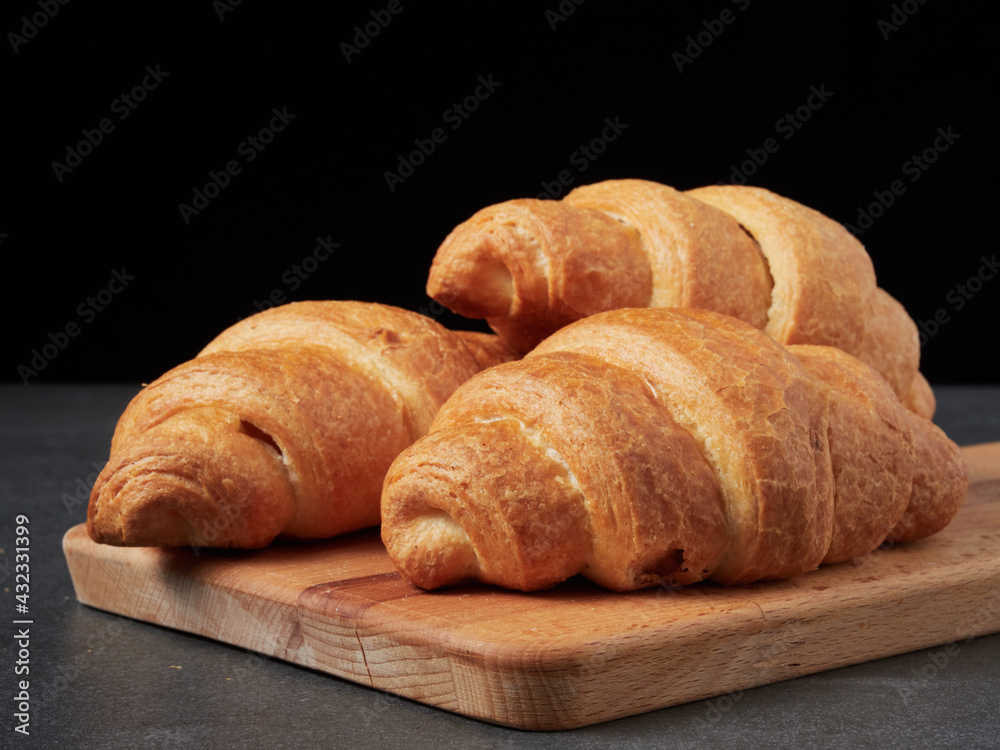 baked french croissants on a brown kitchen board, black background, close-up