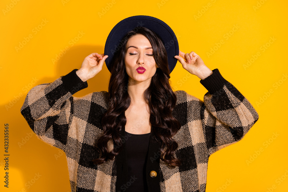 Photo of flirty attractive young woman hold hands hat send air kiss wear plaid coat isolated on yellow color background Photo of flirty attractive young woman hold hands hat send air kiss wear plaid coat isolated on yellow color background