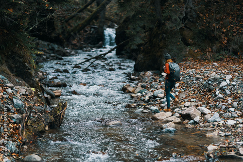 woman hiker with a backpack on the river bank and the forest in the distance tall trees