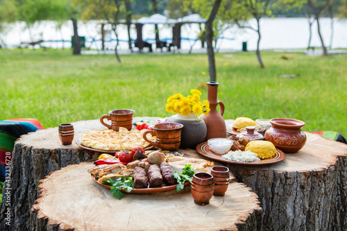 Homemade Romanian Food with grilled meat, polenta and vegetables Platter on camping. Romantic traditional Moldavian food outside on the wood table.