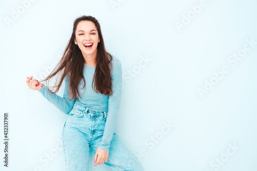 Young beautiful smiling female in trendy summer hipster clothes. Sexy carefree woman posing near light blue wall in studio. Positive model having fun indoors. Cheerful and happy