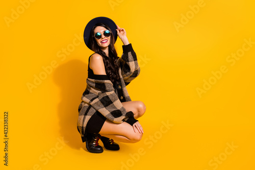 Full length profile photo of gorgeous person sit arm touch headwear wear plaid isolated on yellow color background