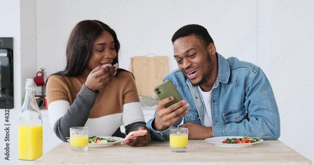 African American couple showing and discussing over mobile phone while having lunch at home African American couple showing and discussing over mobile phone while having lunch at home