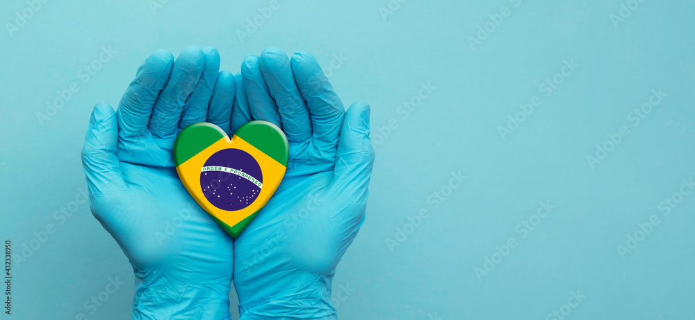 Fototapeta premium Doctors hands wearing surgical gloves holding Brazil flag heart