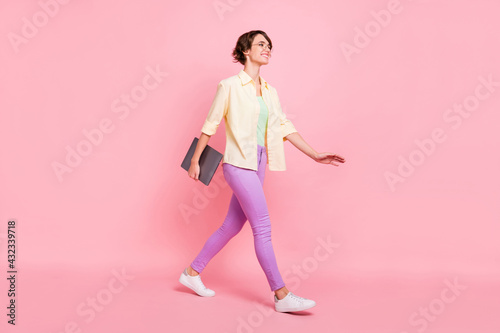 Photo of sweet young woman wear yellow shirt glasses walking holding modern device looking empty space isolated pink color background