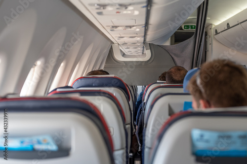 Interior of commercial airplane with unrecognizable passengers on their seats during flight shot from the rear of airplane. economy class travel