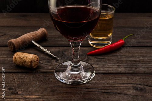 Glass of red wine and tequila with corkscrew and cayenne pepper on an old wooden table. Close up view, focus on the glass of red wine