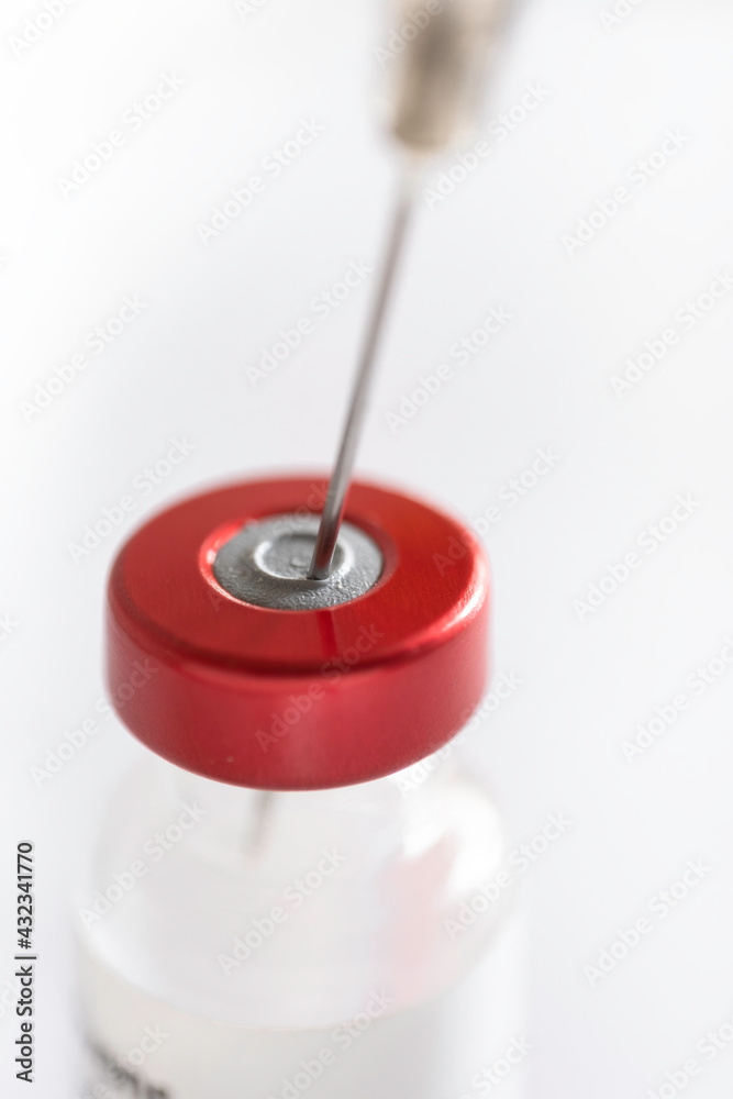 Syringe needle protrudes through the rubber cap of a vaccine vial with red cap. Focus on the rubber stopper, shallow depth of field Syringe needle protrudes through the rubber cap of a vaccine vial with red cap. Focus on the rubber stopper, shallow depth of field