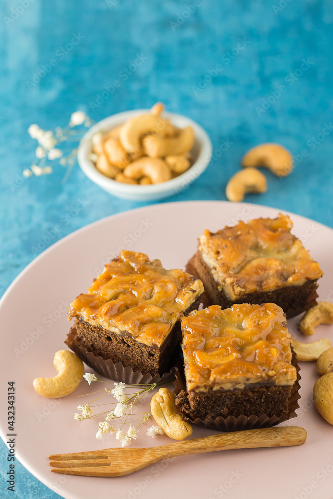 Square toffee cake and cashew nuts are blended with natural honey. On a ceramic plate on a patterned background.