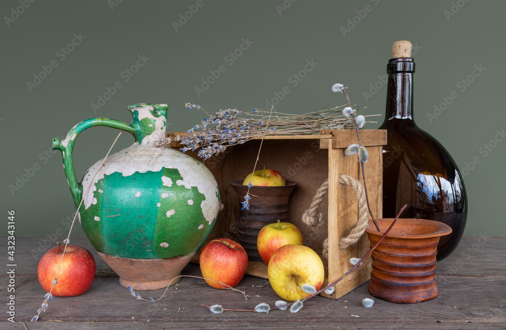 Still life with an old ceramic jug with peeling paint, a large dark brown glass bottle, a ceramic vase, a bunch of lavender and ripe apples. Vintage.