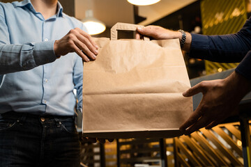 Man in shirt picking a takeaway food bag from a luxury restaurant. Blank craft paper box with room for text or logo.