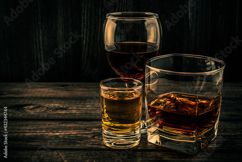 Three glasses with brandy, tequila and red wine on an old wooden table. Angle view