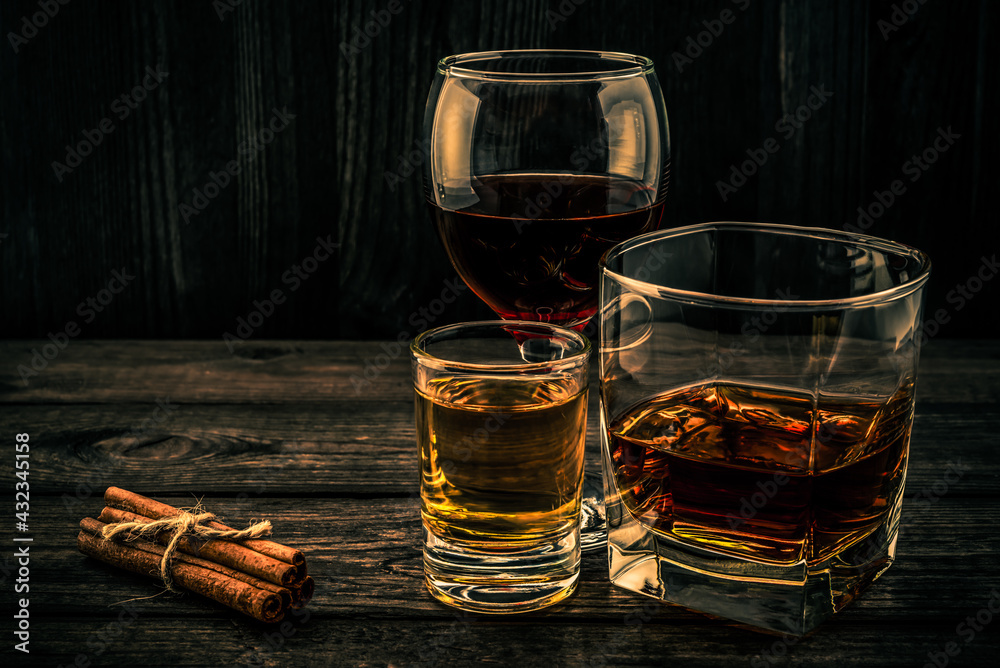 Three glasses with brandy, tequila and red wine with cinnamon sticks tied with jute rope on an old wooden table. Angle view