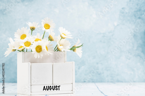 cube calendar for August with daisy flowers over blue background