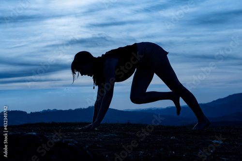 Silhouette of a young woman practicing yoga alone on the mountains with a beautiful Silhouette of a young woman practicing yoga alone on the mountains with a beautiful twilight