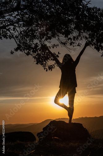 Silhouette of a  young woman practicing yoga on the mountains with a beautiful sunset