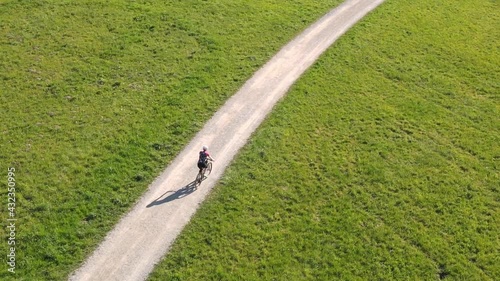 Woman cycling along dirt road across the meadow.