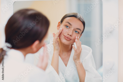 Young caucasian woman doing facebuilding yoga facial gymnastics self lymph facelift massage at home mirror.