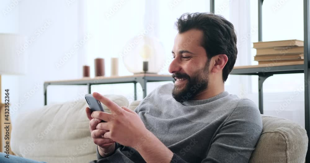 Happy young man text messaging mobile phone at home