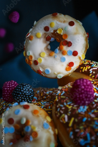 White and brown donuts decorated sprinkles, pink and black gelatin raspberry, levitation, low-key lighting