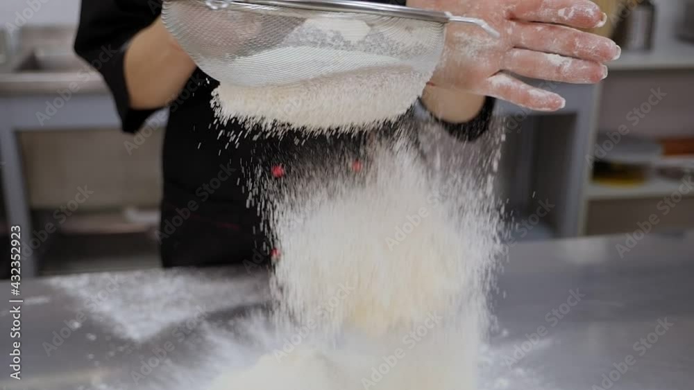 Close-up of a female cook sifting flour through a sieve in the kitchen. Close-up of a female cook sifting flour through a sieve in the kitchen.