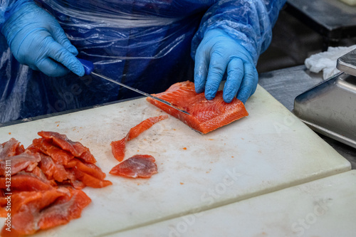 The process of manual filleting of red fish. The worker cuts the fish into pieces with a knife.