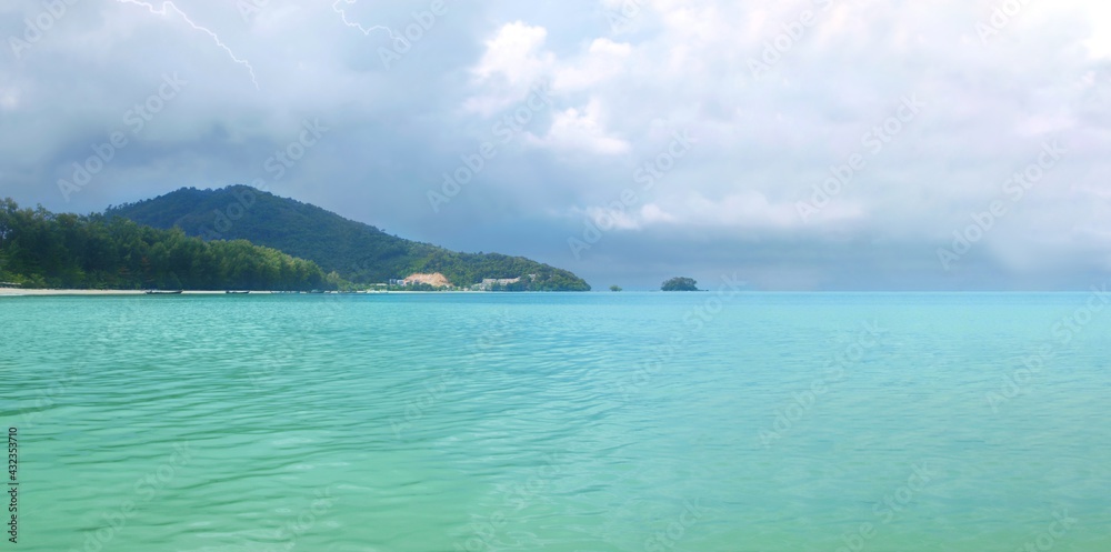 Tropical island, sea bay Wide panorama. Thailand, Phuket. Monsoon season. Sandy coast line. Hills covered with rainforest. Thunderstorm, lightning. Rainy weather. Turquoise clear sea water. Cloudy sky