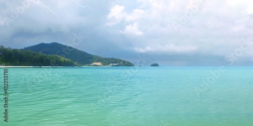 Tropical island, sea bay Wide panorama. Thailand, Phuket. Monsoon season. Sandy coast line. Hills covered with rainforest. Thunderstorm, lightning. Rainy weather. Turquoise clear sea water. Cloudy sky