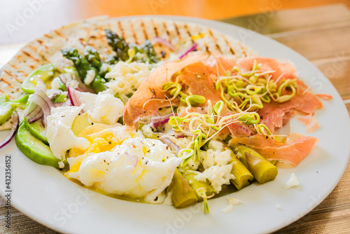 Spring salad with avocado, onion, green asparagus, boiled egg, sunflower sprouts, mozzarella cheese, and Parma ham. Plate on a wooden old kitchen board..View from above..