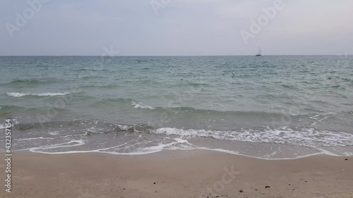 Seagulls and a sailing ship on the sea waves. Stormy weather. Stormy sea. Foamy water on sandy shore.