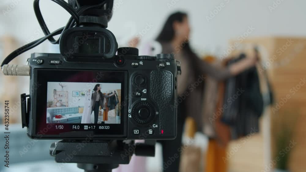 Close-up of digital videocamera screen showing Asian female stylist making video for internet vlog holding garments indoors in apartment. Fashion and blogging concept. Close-up of digital videocamera screen showing Asian female stylist making video for internet vlog holding garments indoors in apartment. Fashion and blogging concept.