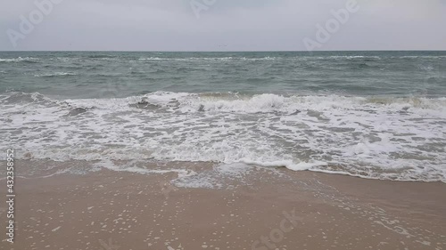 Seascape, sand, sea and gray clouds, seagulls soar above the waves. Stormy weather. Stormy sea.