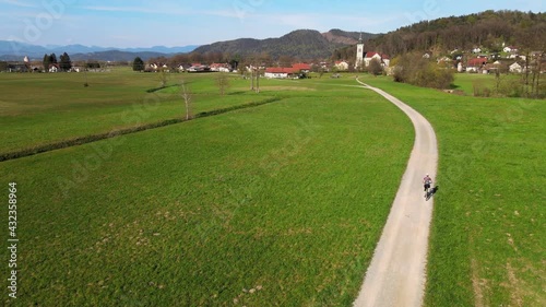 Woman cycling along dirt road across the Slovenian meadow.